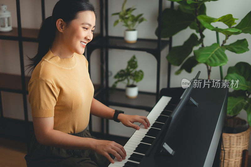 Asian woman learning to play the piano watching video clips from tablet.